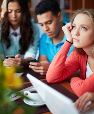 Portrait of teenage friends using modern gadgets while sitting in cafe, focus on pensive girl